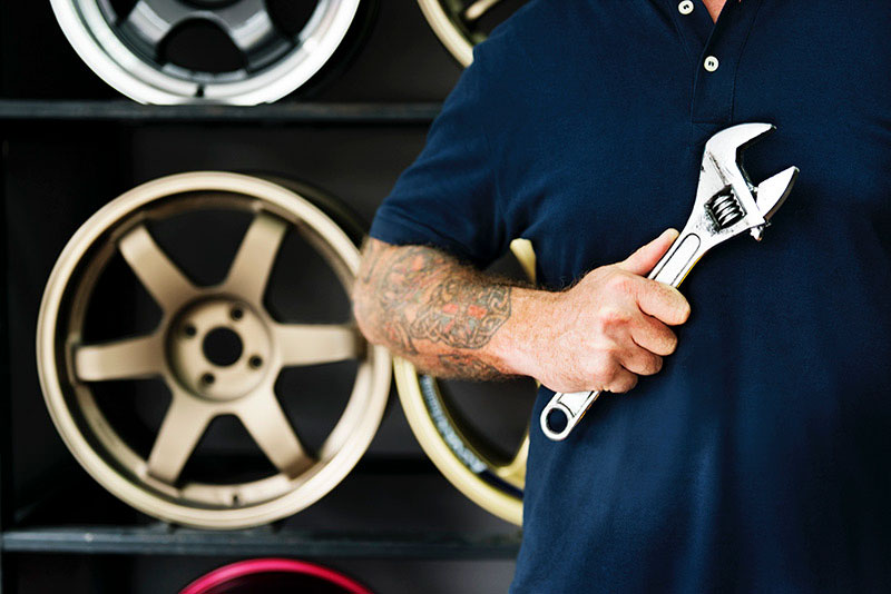 Closeup torso image of man holding wrench with tire rims in background
