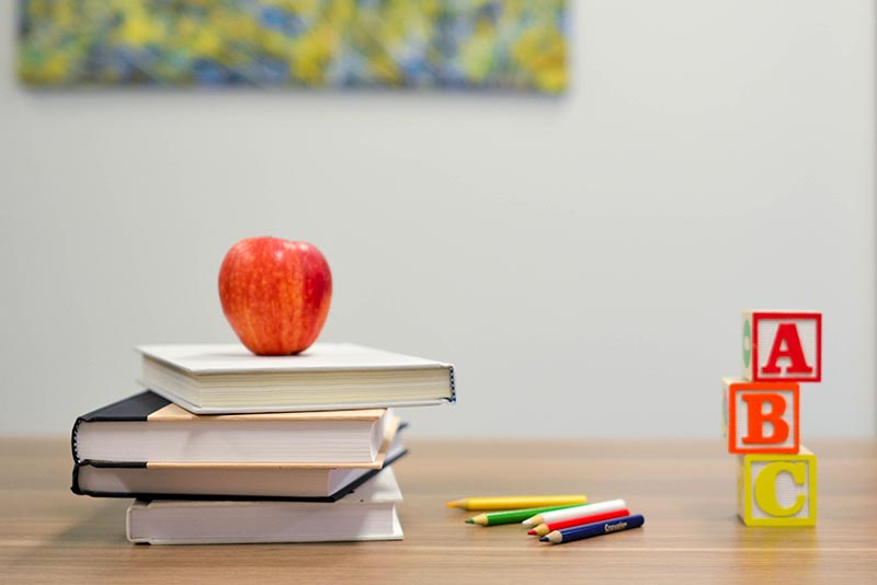 Image of apple on stacked books, coloring pencils and ABC blocks